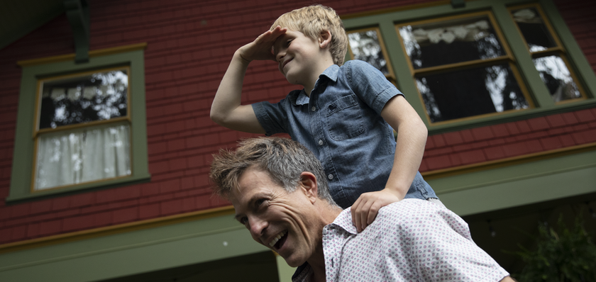 Father with his son on his shoulders in front of their home